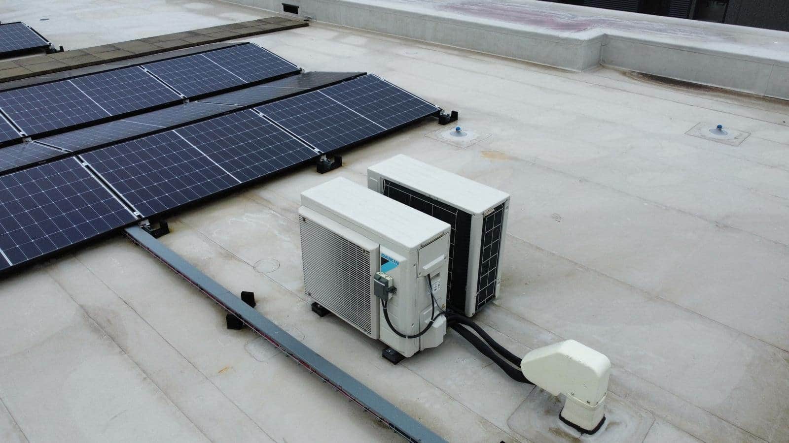 Twee airco-buitenunits naast zonnepanelen op een plat dak.