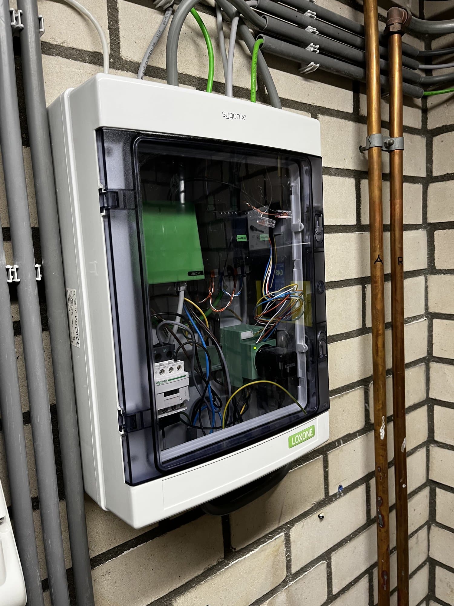 Opbouwkast met Loxone-componenten en invoerende bekabeling op een gemetselde wand.