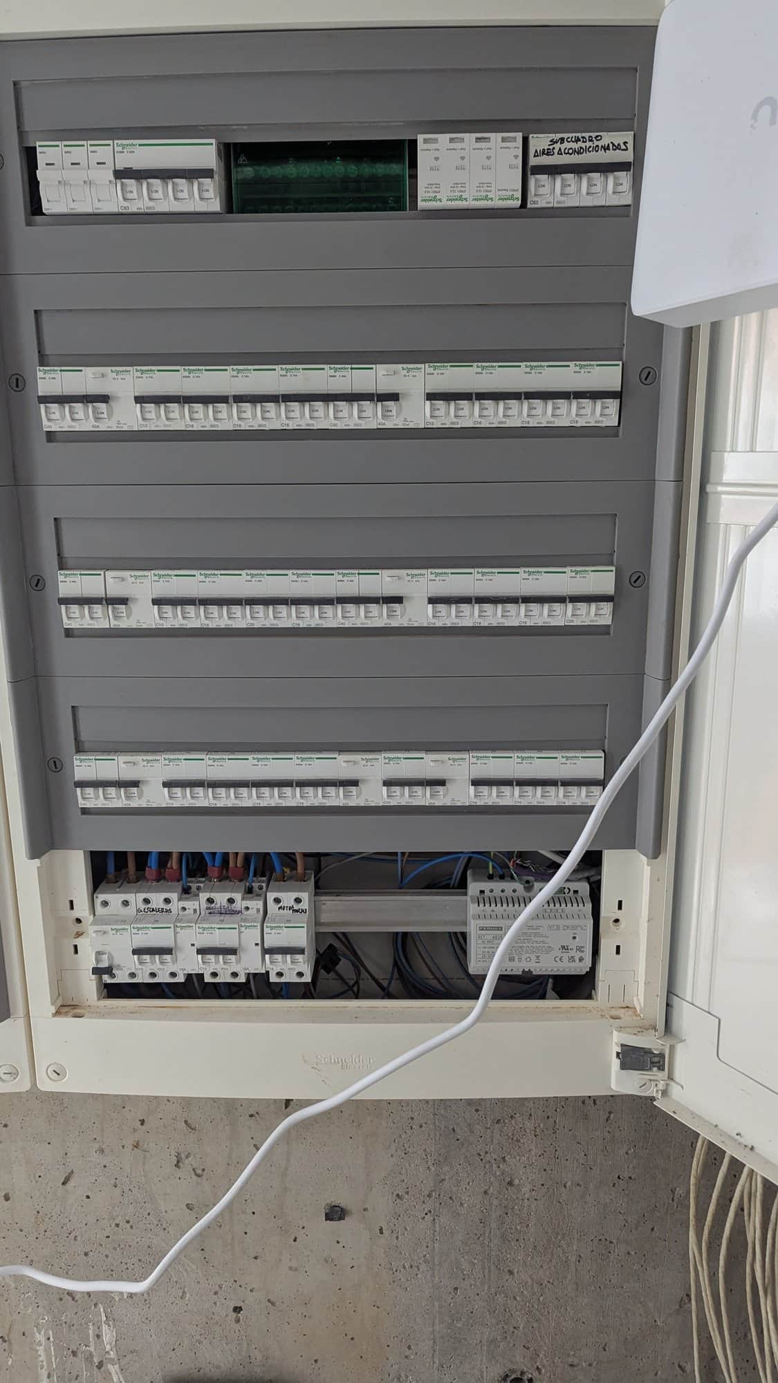 Geopende verdeelkast met rijen installatieautomaten op een betonnen wand.