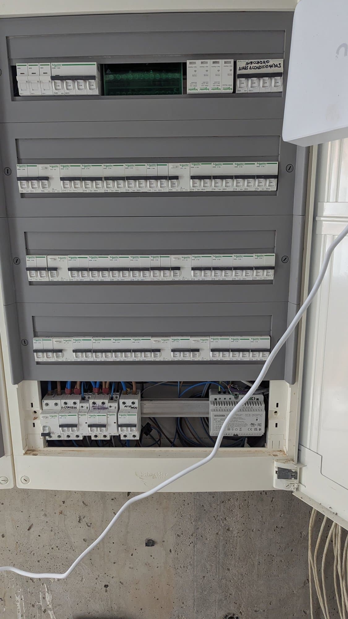 Geopende verdeelkast met rijen installatieautomaten op een betonnen wand.